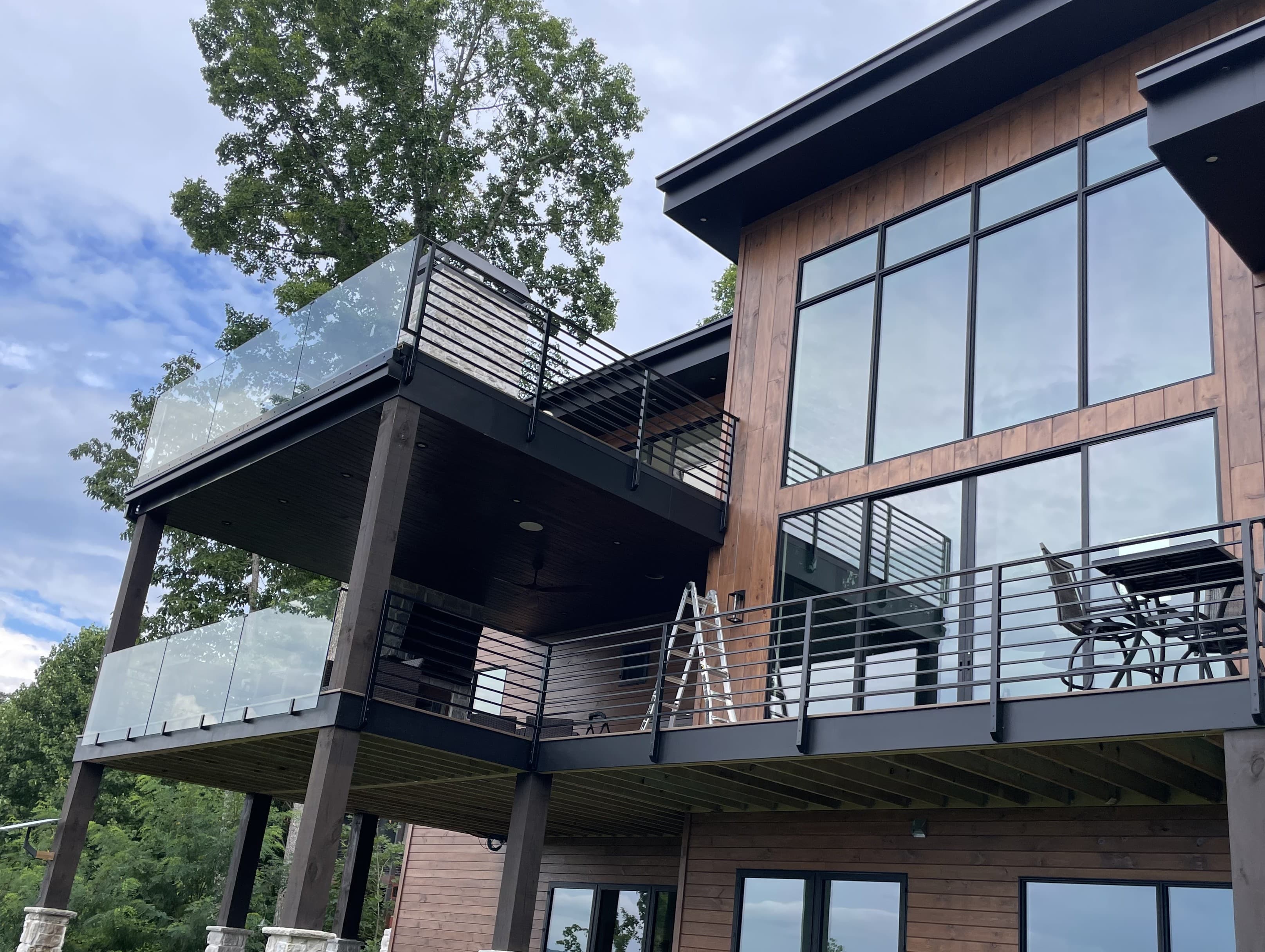 Exterior glass railing with clear panels and metal hardware along a deck edge.