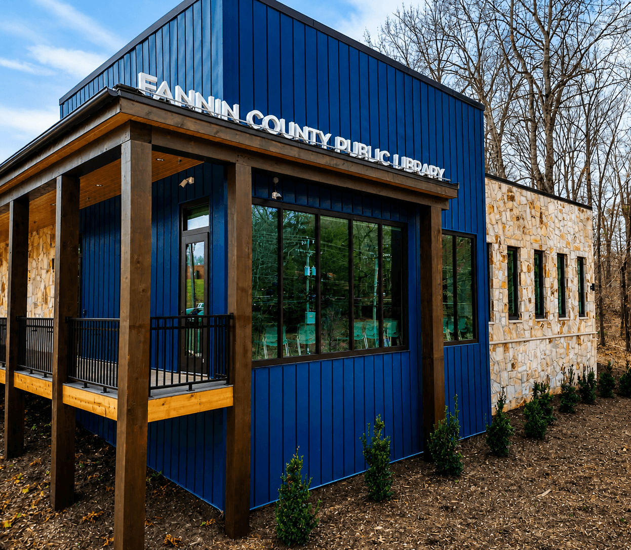 Fannin County Public Library exterior—blue siding, stone walls, large black-framed glazing, and building signage.