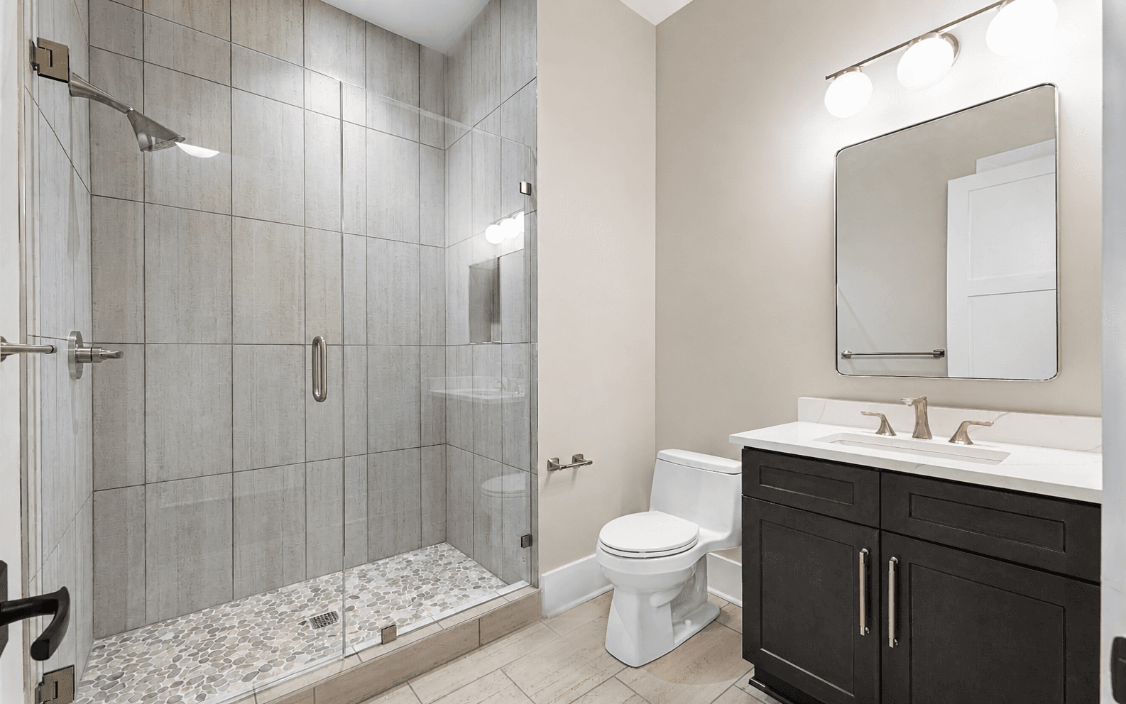 Modern bathroom with frameless glass shower, vanity with brushed metal pulls and faucet, and coordinated bath hardware.