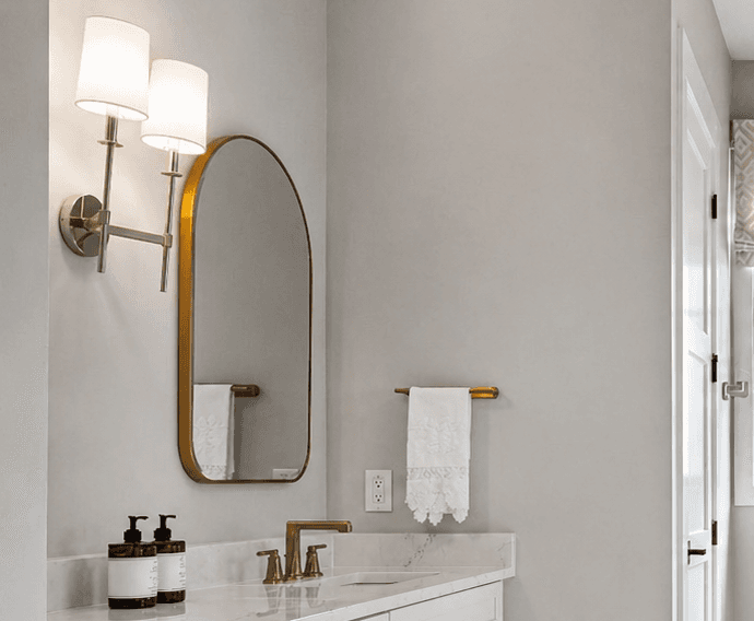 Bathroom vanity with an arched gold-framed custom mirror, marble counter, and brass faucet.