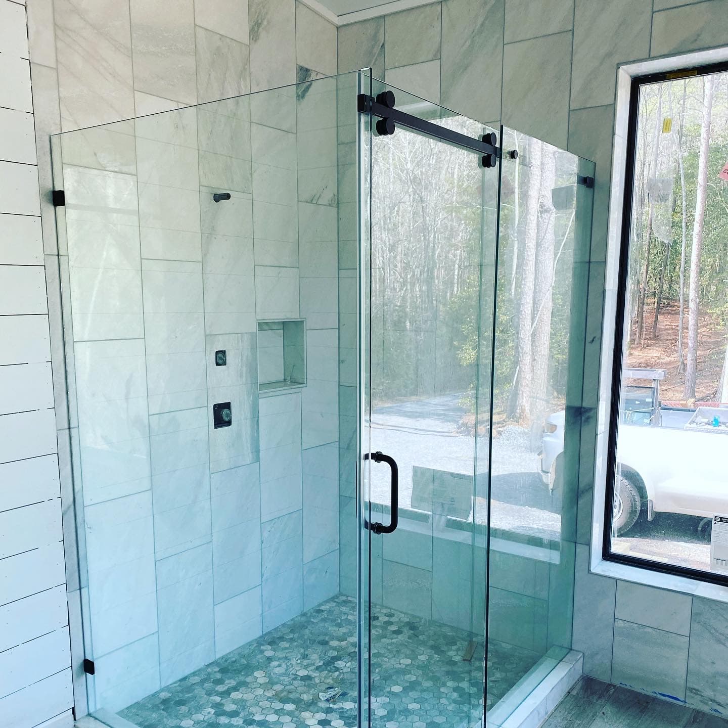 Frameless sliding glass shower door with matte black hardware and marble tile.