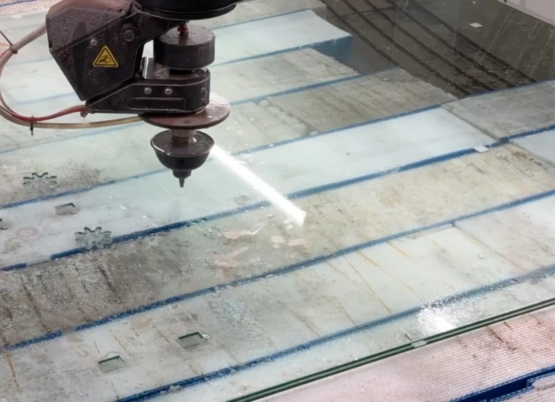 Close-up of TVS waterjet glass cutting, with shaped openings and rectangular cutouts visible in the sheet.