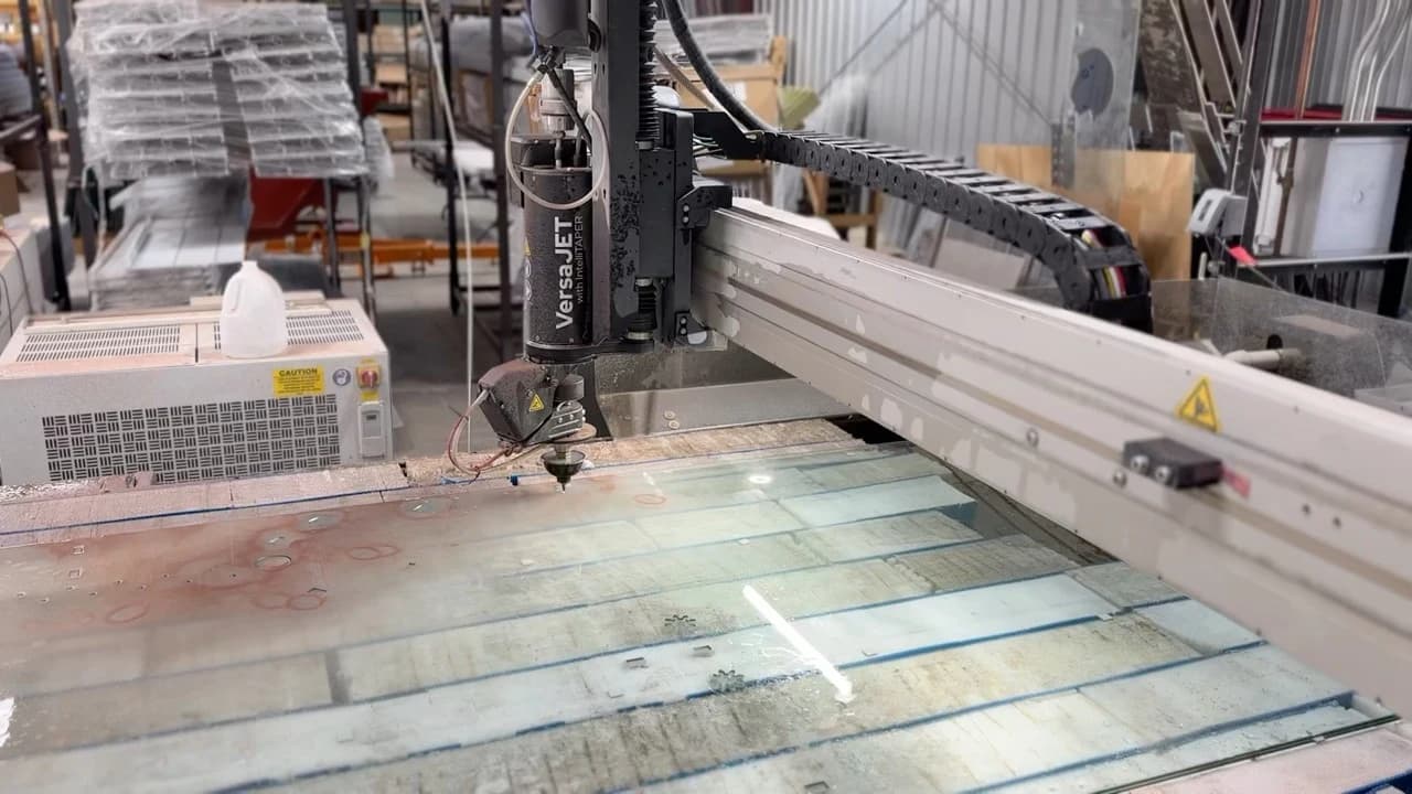 TVS waterjet cutting table with an OMAX VersaJET head positioned over a glass sheet.